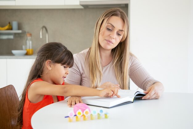 Cute little girl pointing at text and learning with mom.