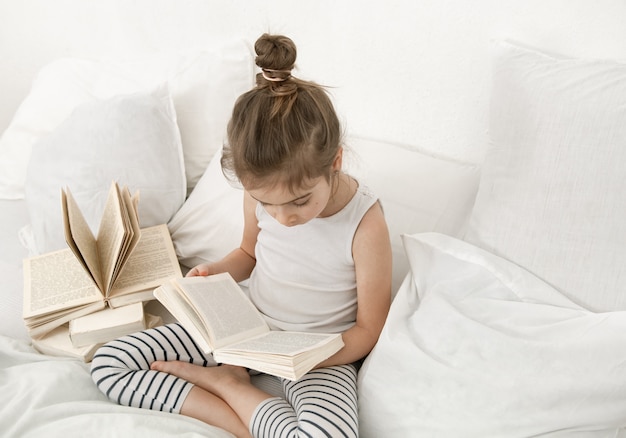 Bambina sveglia che legge un libro sul letto in camera da letto.