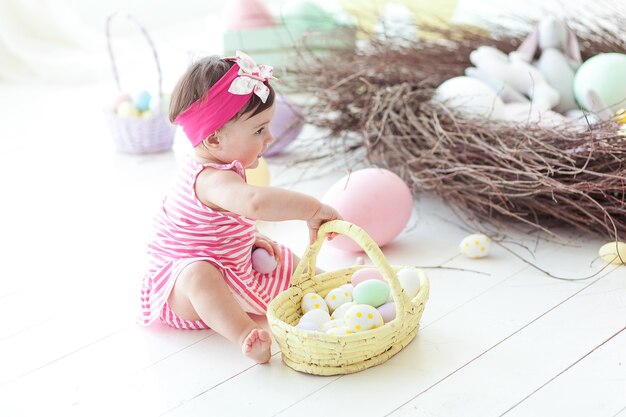 Cute little girl in red dress with Easter eggs sitting on floor at home.