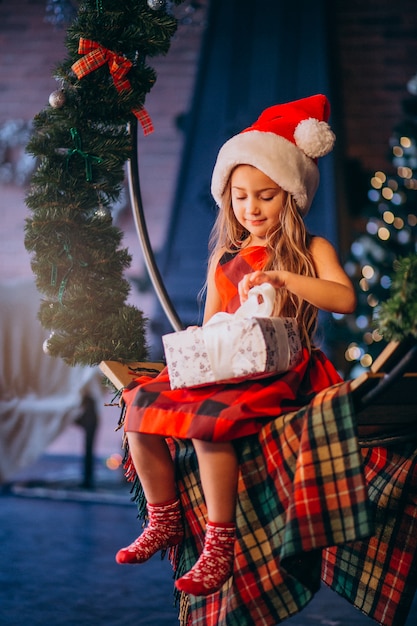 Милая маленькая девочка в шляпе Санты распаковывая подарок на рождество