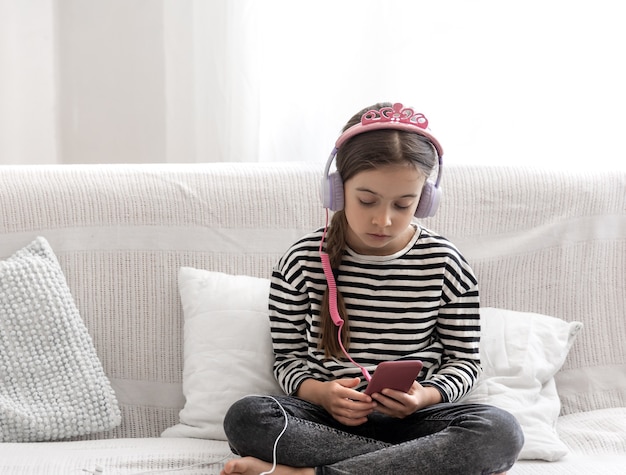 A cute little girl sits at home on the couch and listens to music with headphones