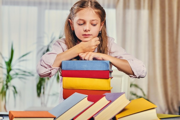 Cute little girl at the table with a lot of colorful books.