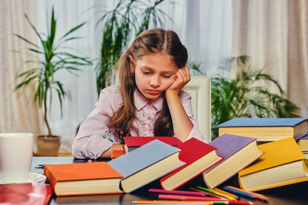 Cute little girl at the table with a lot of colorful books.