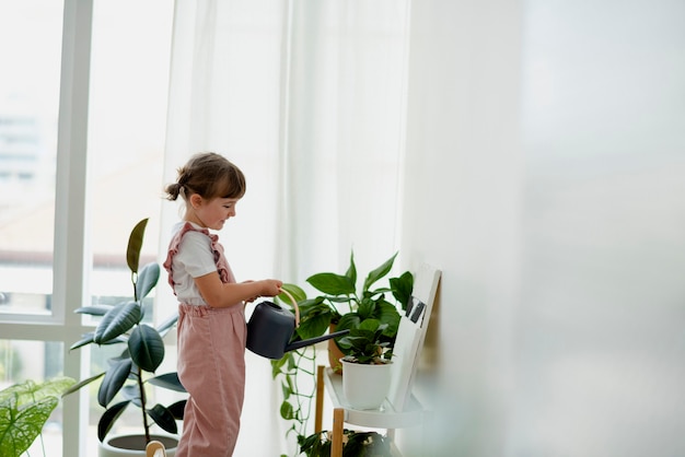 Милая маленькая девочка поливает растения дома