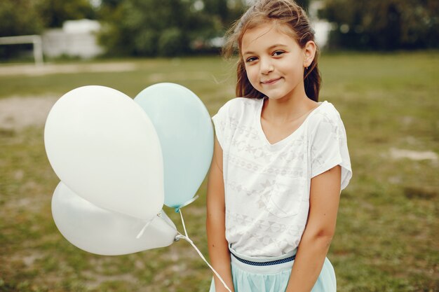 白いTシャツと青いスカートのかわいい女の子は風船で夏の公園で遊ぶ