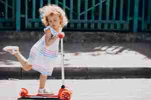 Free photo cute little girl with curly park riding scooter