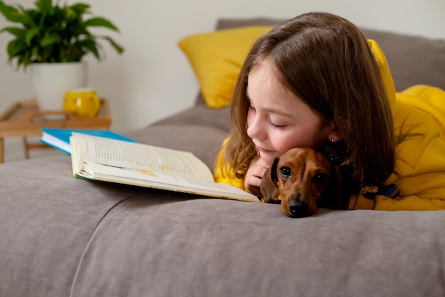 Cute little girl with a dwarf dachshund are lying on the bed and reading a book