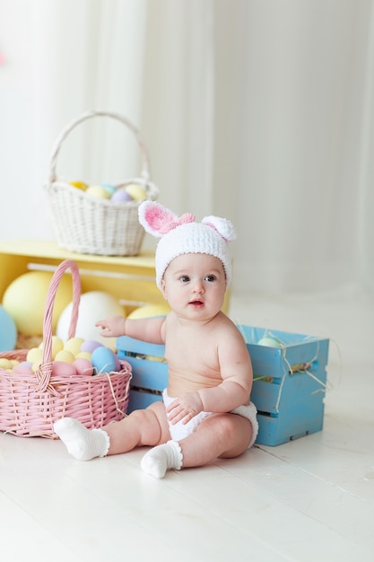 Bambina sveglia con le uova di pasqua che si siedono sul pavimento a casa.