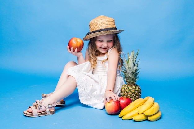 Милая маленькая девочка с фруктами, изолированные на синей стене