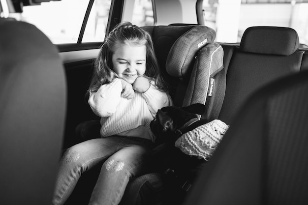 Free photo cute little girl with her pet sitting in the back of a car