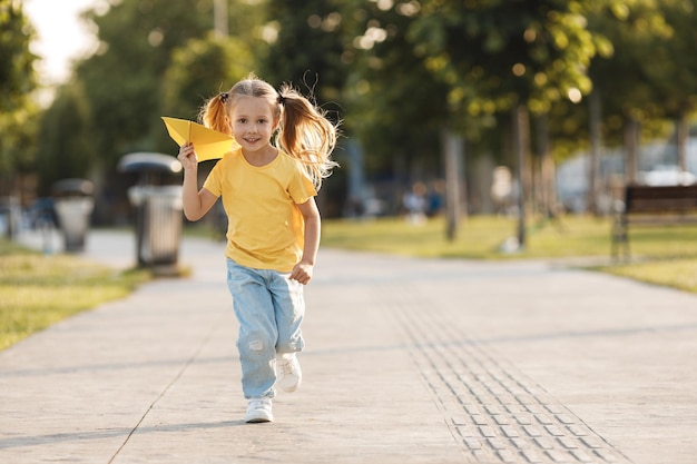 Foto gratuita bambina carina con aereo di carta all'aperto