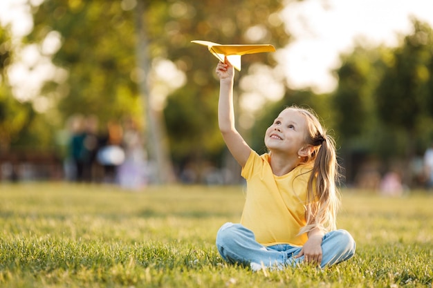 Foto gratuita bambina carina con aereo di carta all'aperto