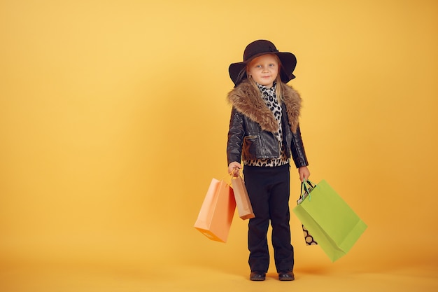 Cute little girl with shopping bags on a yellow background