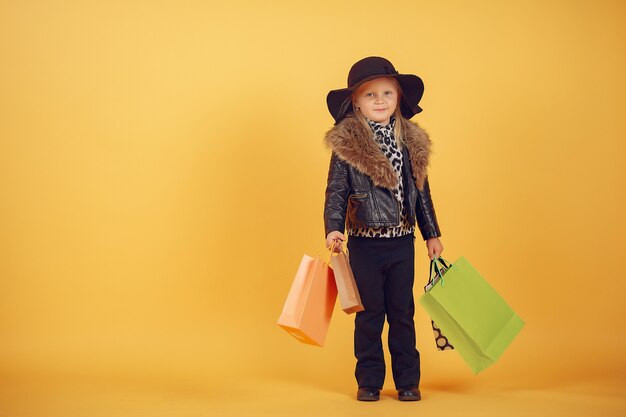 Cute little girl with shopping bags on a yellow background