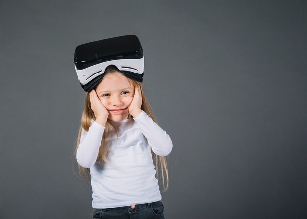 Милая маленькая девочка с очки виртуальной реальности на голове, держа ее щеки