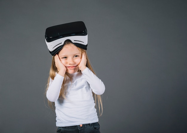 Cute little girl with virtual reality glasses on head holding her cheeks