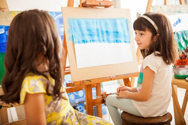 Милые маленькие девочки сравнивают работы друг друга и делятся идеями для своего художественного класса в школе.