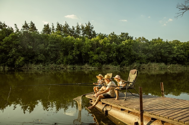 Симпатичные маленькие девочки и их дедушка на рыбалке на озере или реке