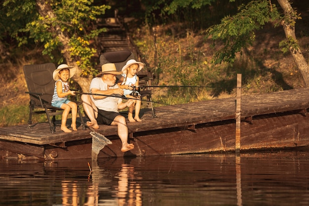 귀여운 소녀들과 할아버지가 호수 나 강에서 낚시를하고 있습니다.
