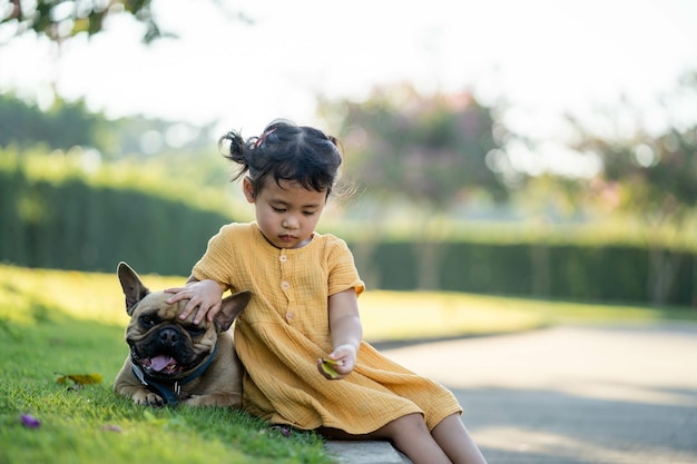 Piccola ragazza sveglia del sud-est asiatico che si siede in un parco con il suo bulldog francese