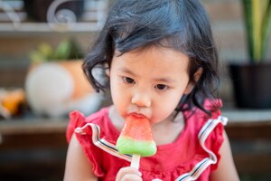 Миленькая тайская девочка ест мороженое со вкусом арбуза