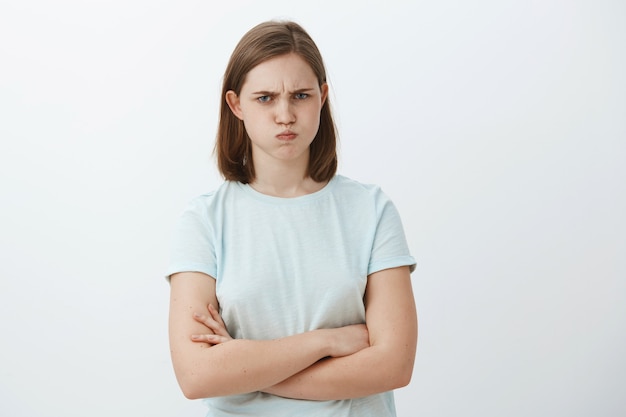 cute mad or offended female with flapped ear sulking and frowning crossing arms on chest standing in insulted pose being displeased or angry at someone over gray wall
