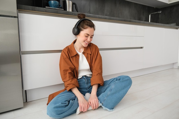 Free photo cute modern girl on kitchen floor at home listening music in wireless headphones having fun