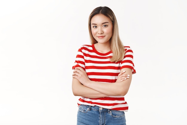 Cute modest asian blong teenage girl sighing watching distance classmate feel sympathy cross fingers chest smiling gently kind speaking look happy shy standing white background striped summer tshirt