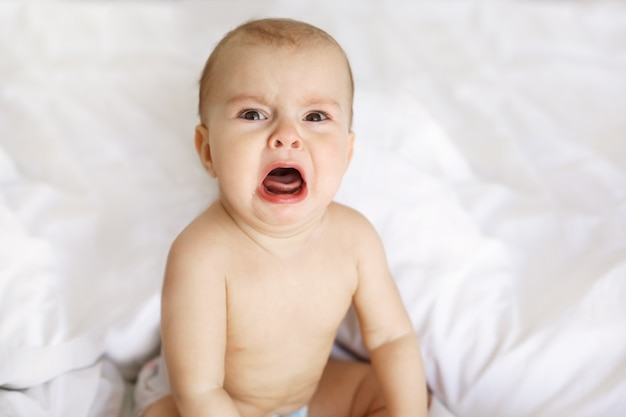 Cute nice little baby woman crying lying with her mom on bed at home.