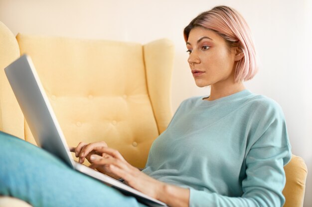 Симпатичная розоволосая студентка с портативным компьютером для онлайн-обучения
