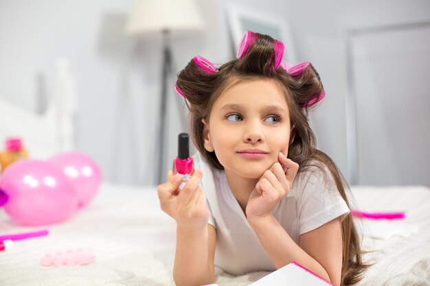 Cute preschooler laying on white blanket holding nail polish.