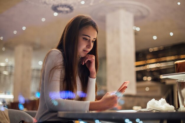 カフェのスマートフォンでキュートでかわいい若い女性