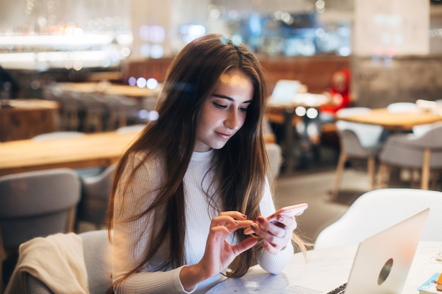 Cute and pretty young woman on smartphone in cafe