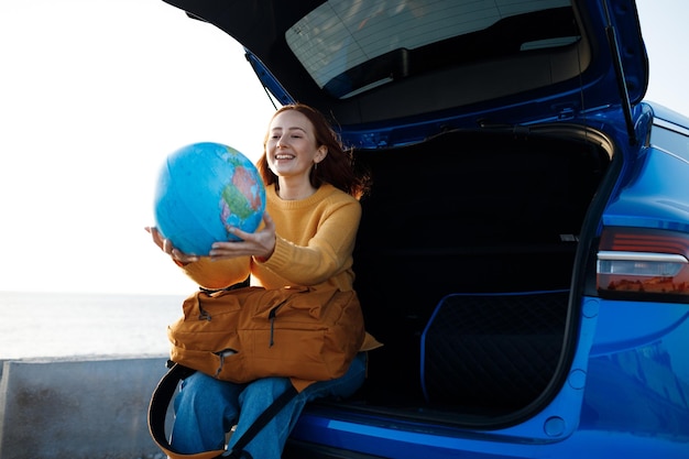 милая рыжеволосая женщина собирается путешествовать с глобусом в машине