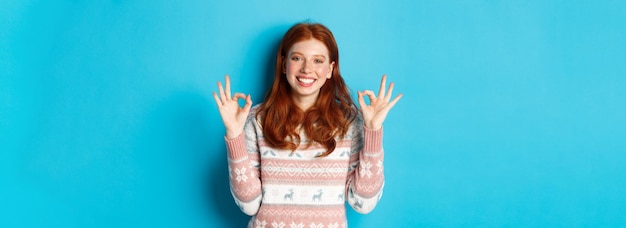 무료 사진 스웨터를 입은 귀여운 빨간 머리 소녀는 만족스러운 미소를 짓고 좋은 채널을 칭찬하는 것을 좋아합니다.