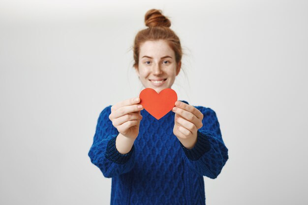 Cute redhead girl showing heart gesture. Relationship and love concept