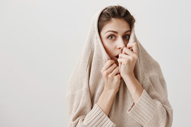 Cute scared girl hiding inside sweater and looking at front frightened