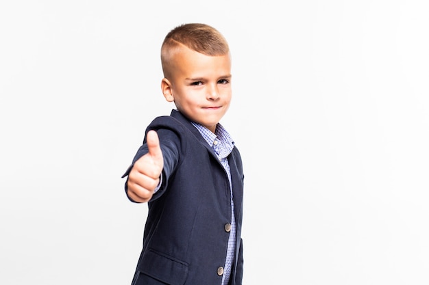 Cute schoolboy making thumbs up sign, isolated on white wall