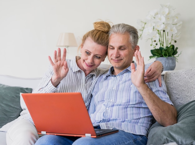 Cute senior couple waving at laptop