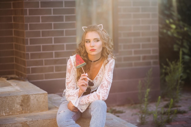 Free photo cute sexy brunette looking away sitting on stairs and eating candy