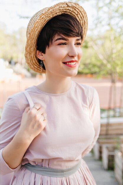 Cute short-haired girl dreamy smiling, looking away during walk in park