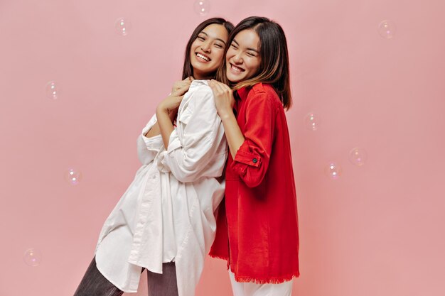 Cute short-haired girls in red and white shirts laugh on pink wall with bubbles