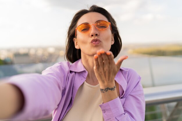 Cute short haired woman in orange sunglasses making self portrait on the bridge