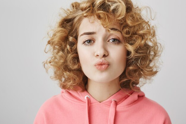Cute shy curly-haired girl folding lips trying to kiss
