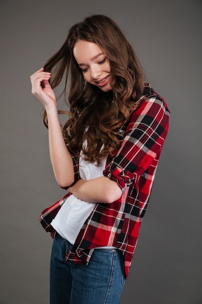 Cute shy young woman standing and tounching her curly hair