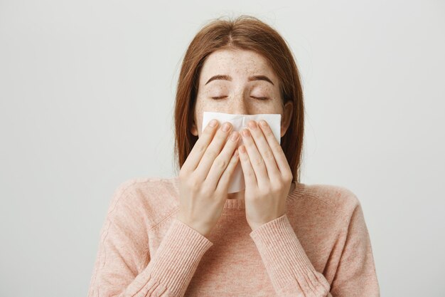 Cute sick redhead girl with allergy sneezing in napkin