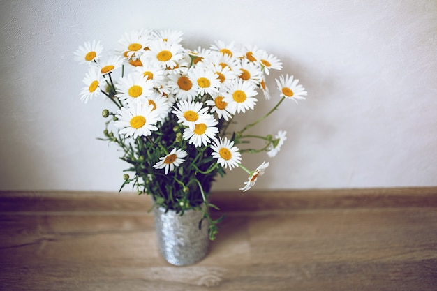 Cute silver vase with white chamomiles in light room and wooden floor . Shabby chic style.