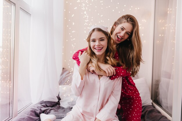 かわいい姉妹は寝室で浮気する流行のパジャマを着ています。朝にエネルギーを表現する驚くべき白人の女の子。