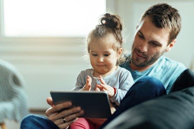 Cute small girl and her father watching cartoons on digital tablet at home