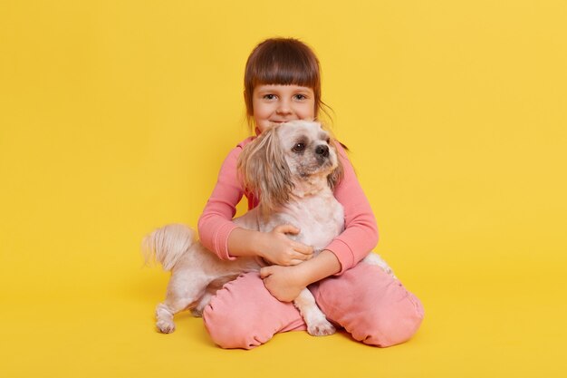 Cute small girl hugging her pet dog isolated on yellow